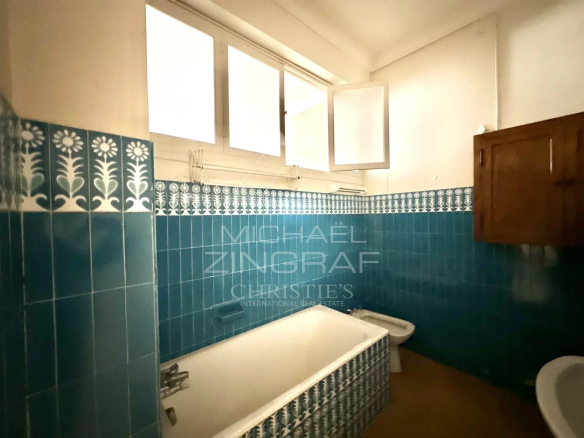 Salle de bain avec baignoire et carrelage bleu, fenêtre ouverte, dans un appartement à Nice.