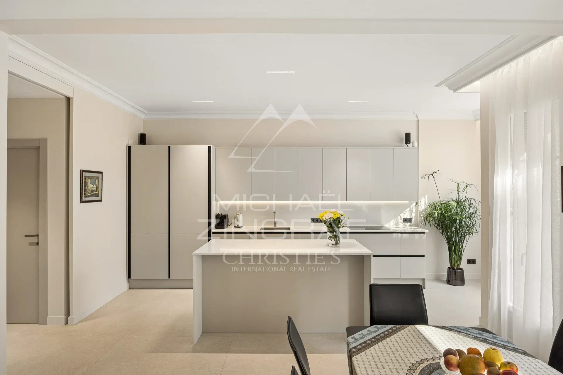 Cuisine moderne et lumineuse d'un appartement rénové avec un îlot central et des meubles clairs.