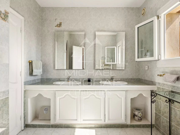 Spacious bathroom with double sink and mirrors, decorated with light-colored tiles.
