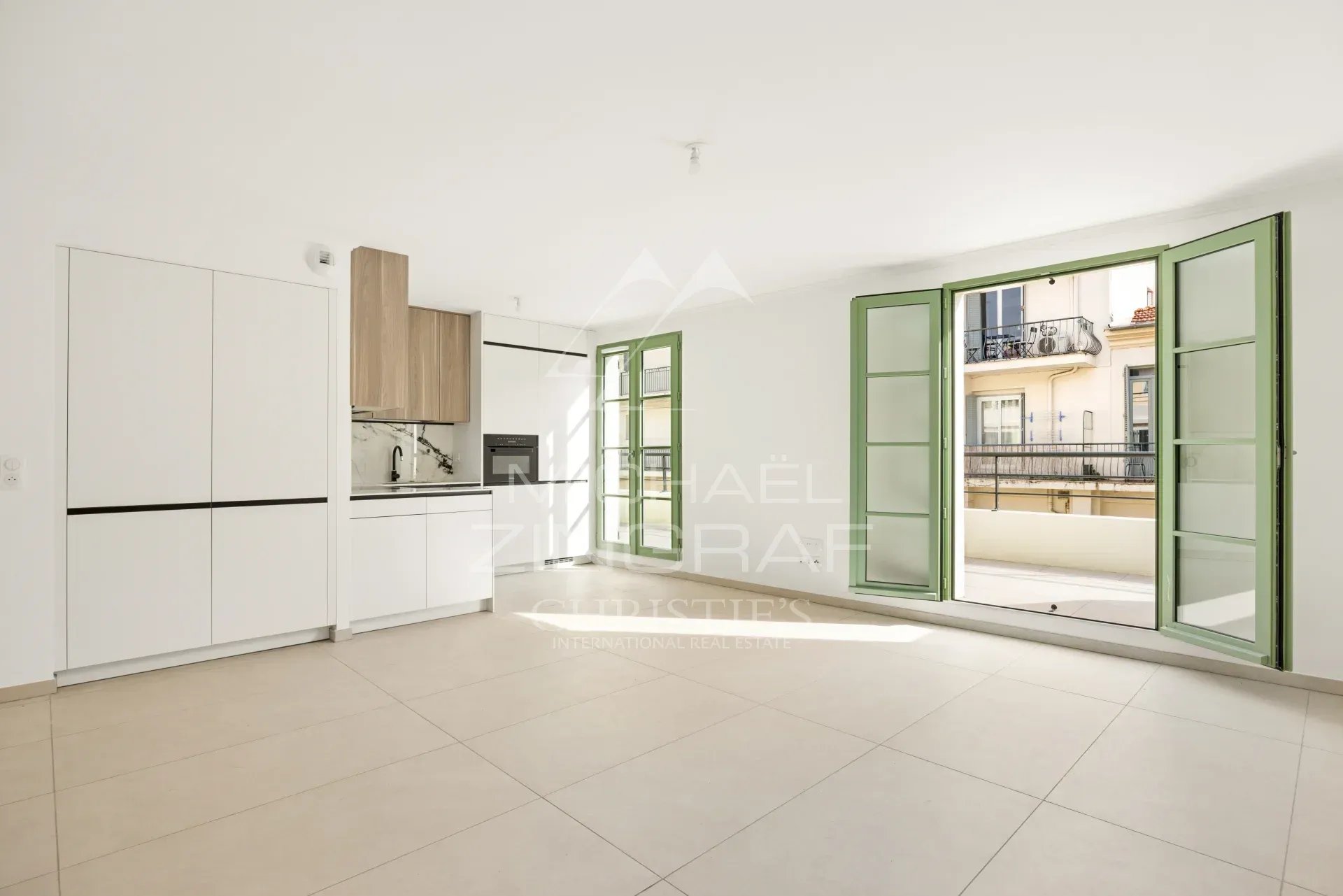 Intérieur d'un appartement neuf à Nice avec fenêtres ouvertes et cuisine intégrée.
