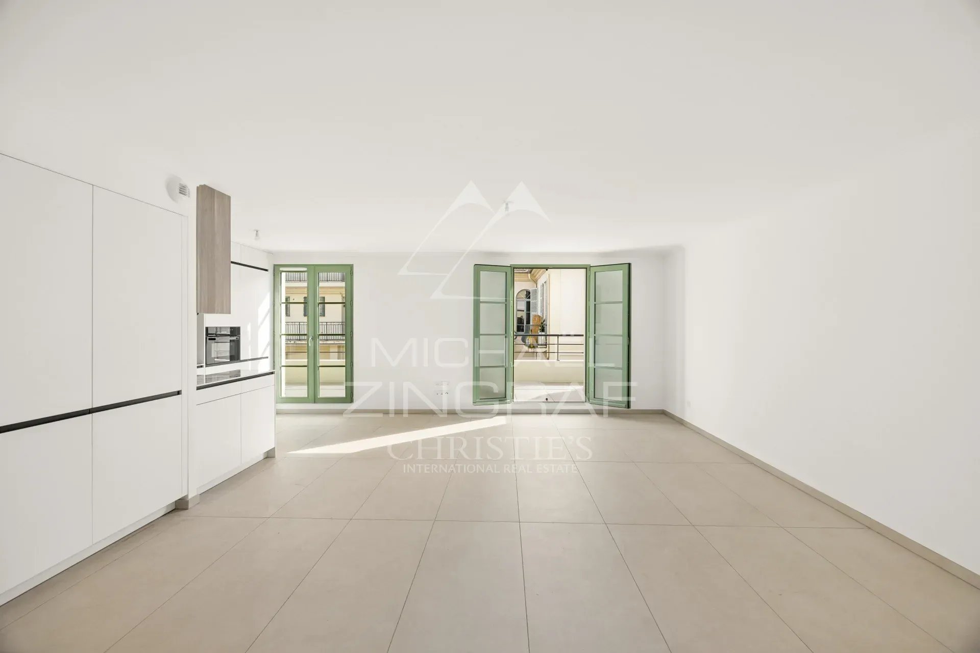 Intérieur d'un appartement moderne et lumineux à Nice, avec fenêtres ouvertes et carrelage clair.