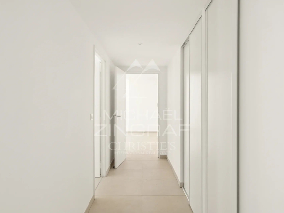 Couloir d'un appartement moderne et lumineux à Nice, murs blancs et sol carrelé.