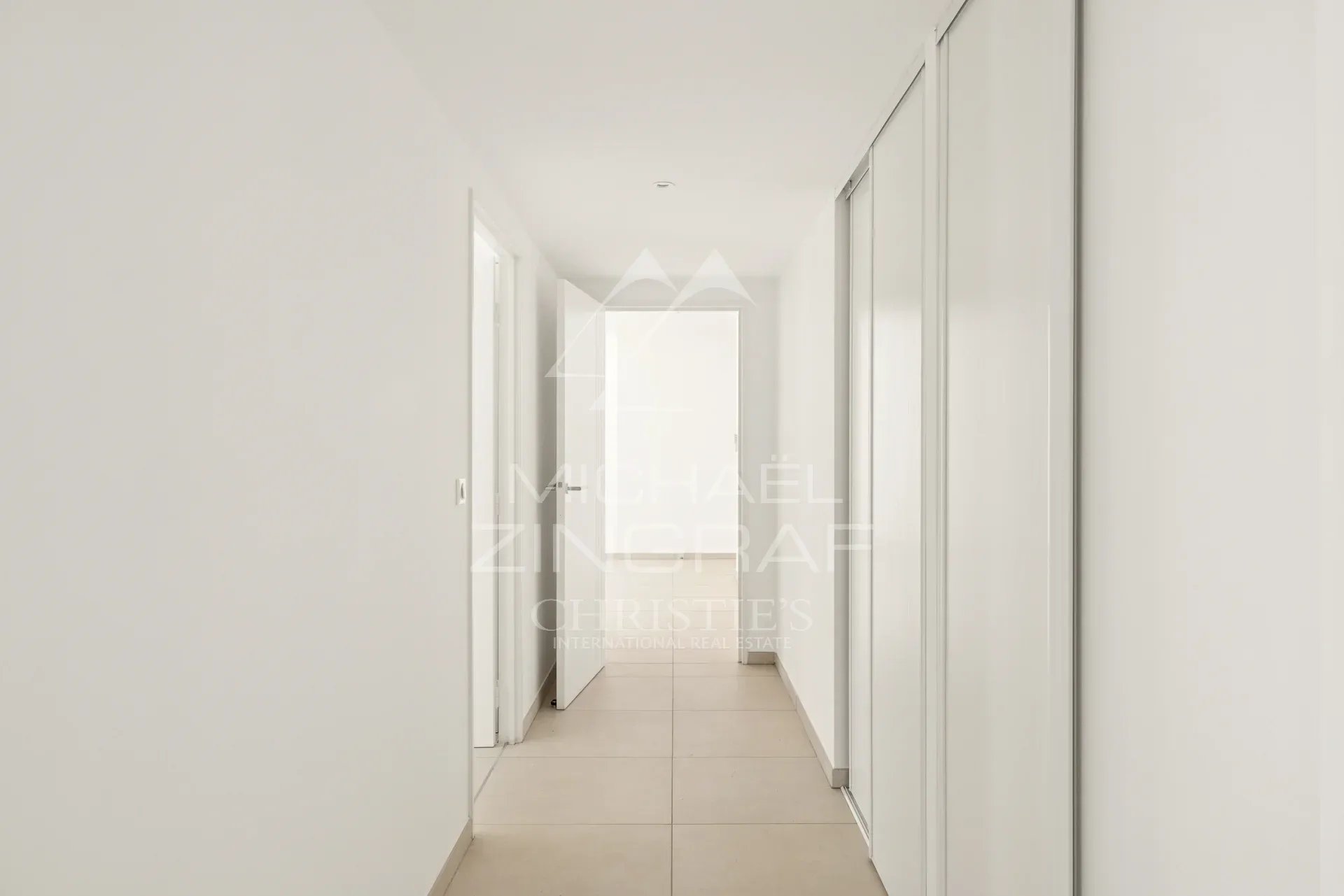 Couloir d'un appartement moderne et lumineux à Nice, murs blancs et sol carrelé.