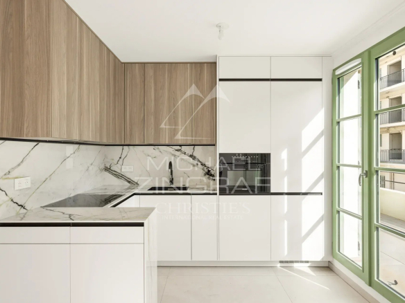 Cuisine moderne avec des meubles blancs et un plan de travail en marbre, fenêtres ouvertes sur un balcon.