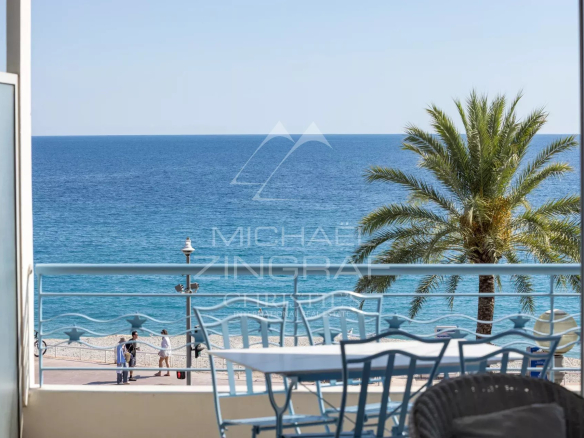 View of the Mediterranean Sea from a terrace with chairs and a table, palm tree in the background.
