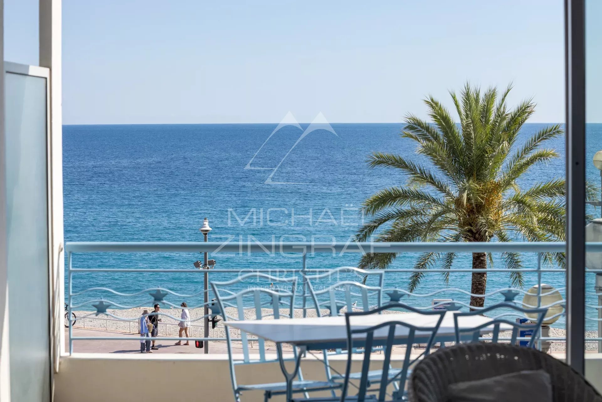 Sea view from the terrace of an apartment in Nice View of the Mediterranean Sea from a terrace with chairs and a table, palm tree in the background.