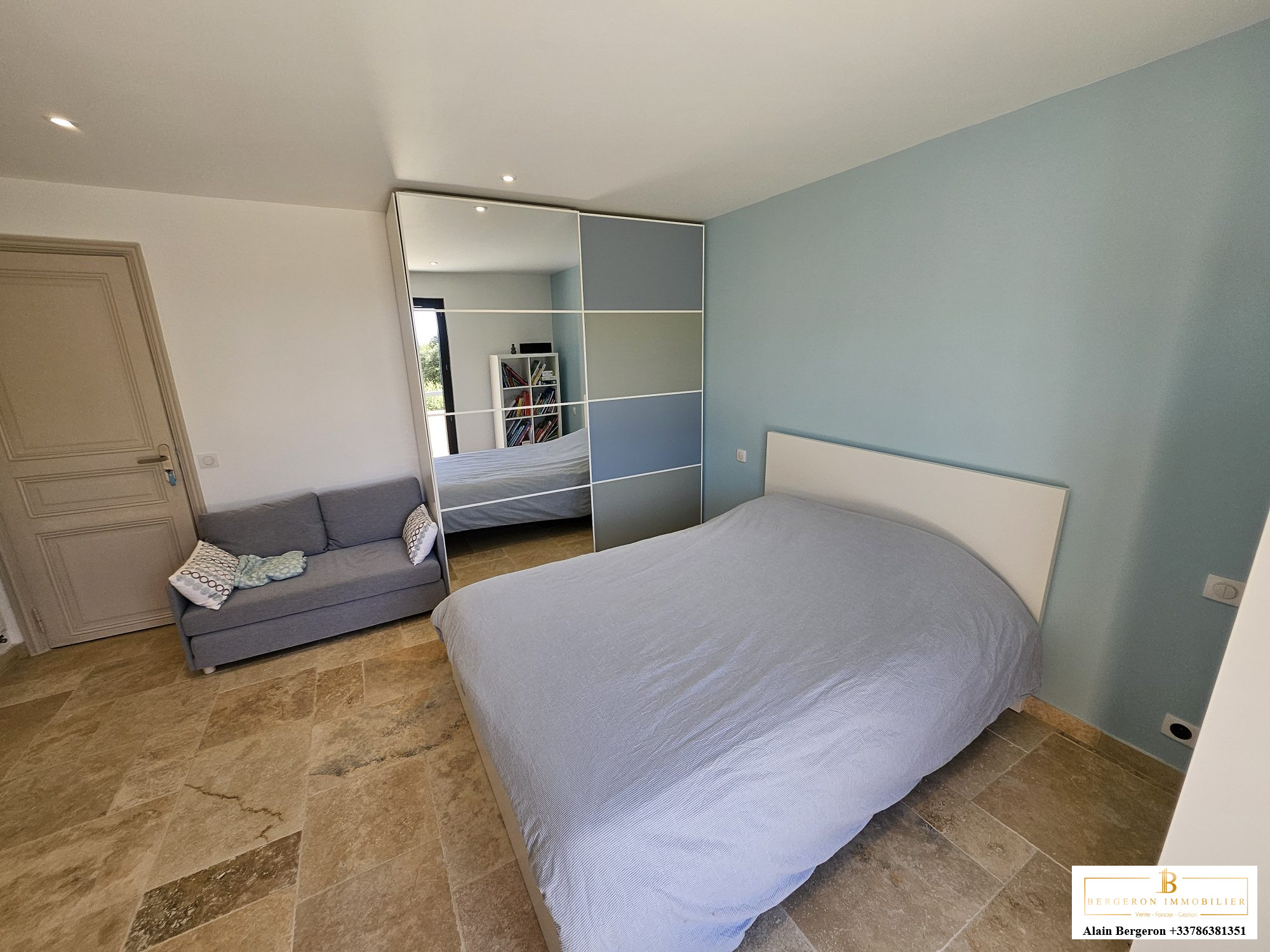 Chambre spacieuse avec lit double et canapé, murs clairs et sol en pierre.