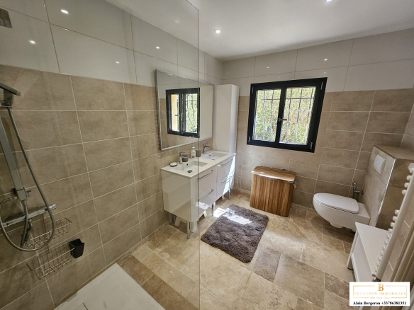 Salle de bain moderne avec douche, lavabo et toilettes, lumière naturelle à travers une fenêtre.