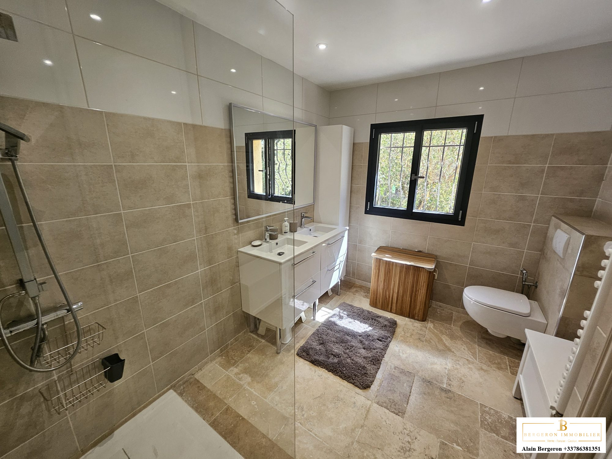 Salle de bain moderne avec douche, lavabo et toilettes, lumière naturelle à travers une fenêtre.