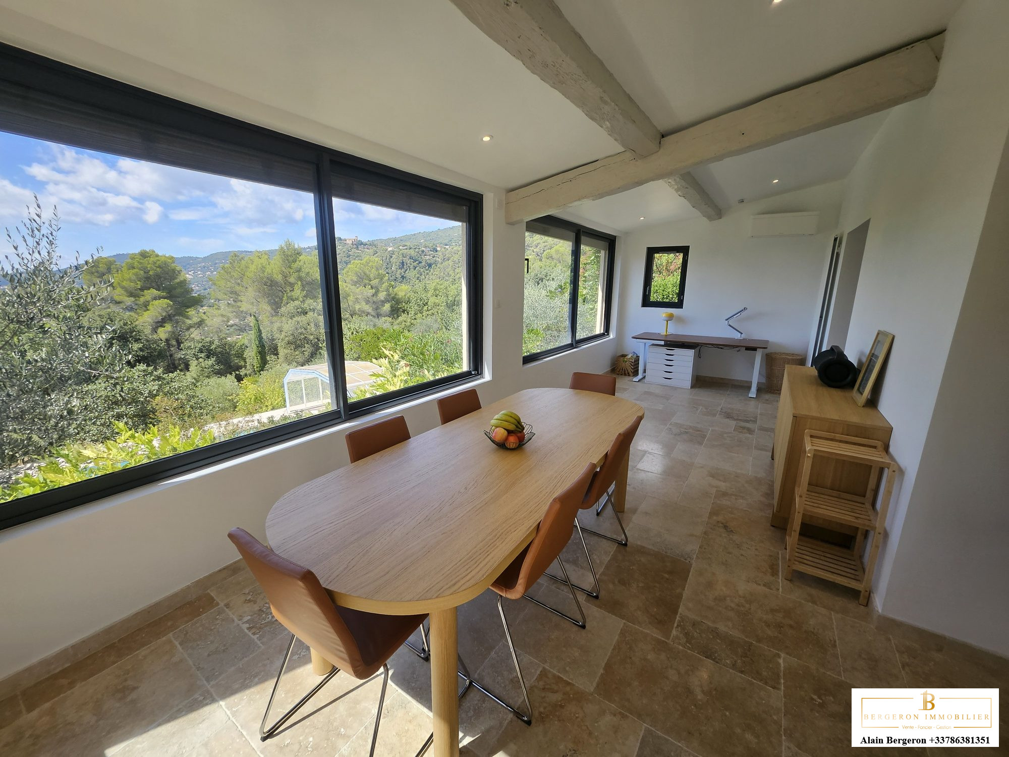 Intérieur d'une maison spacieuse à Cabris avec une grande table et des fenêtres offrant une vue sur la nature.