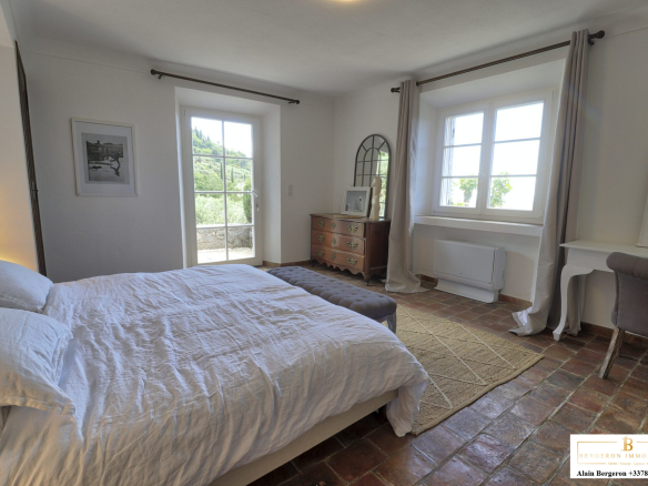 Chambre lumineuse d'une bastide provençale avec lit, fenêtre et mobilier élégant.