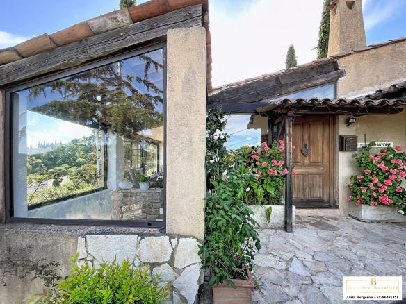 Entrance to a stone house with views of nature, flowers and large bay windows.