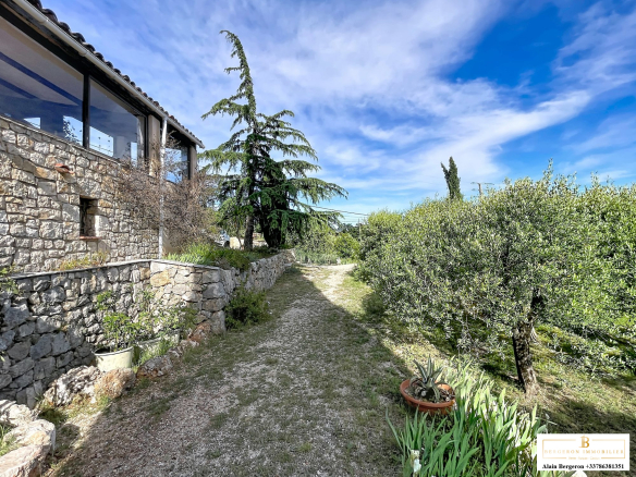 Path leading to a stone house with a sea view, surrounded by trees and greenery.