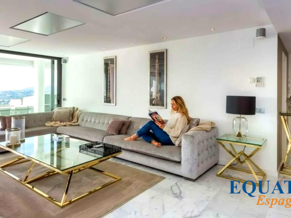 Woman sits on a light gray sectional reading a magazine in a bright, modern living room with a glass-and-gold coffee table.