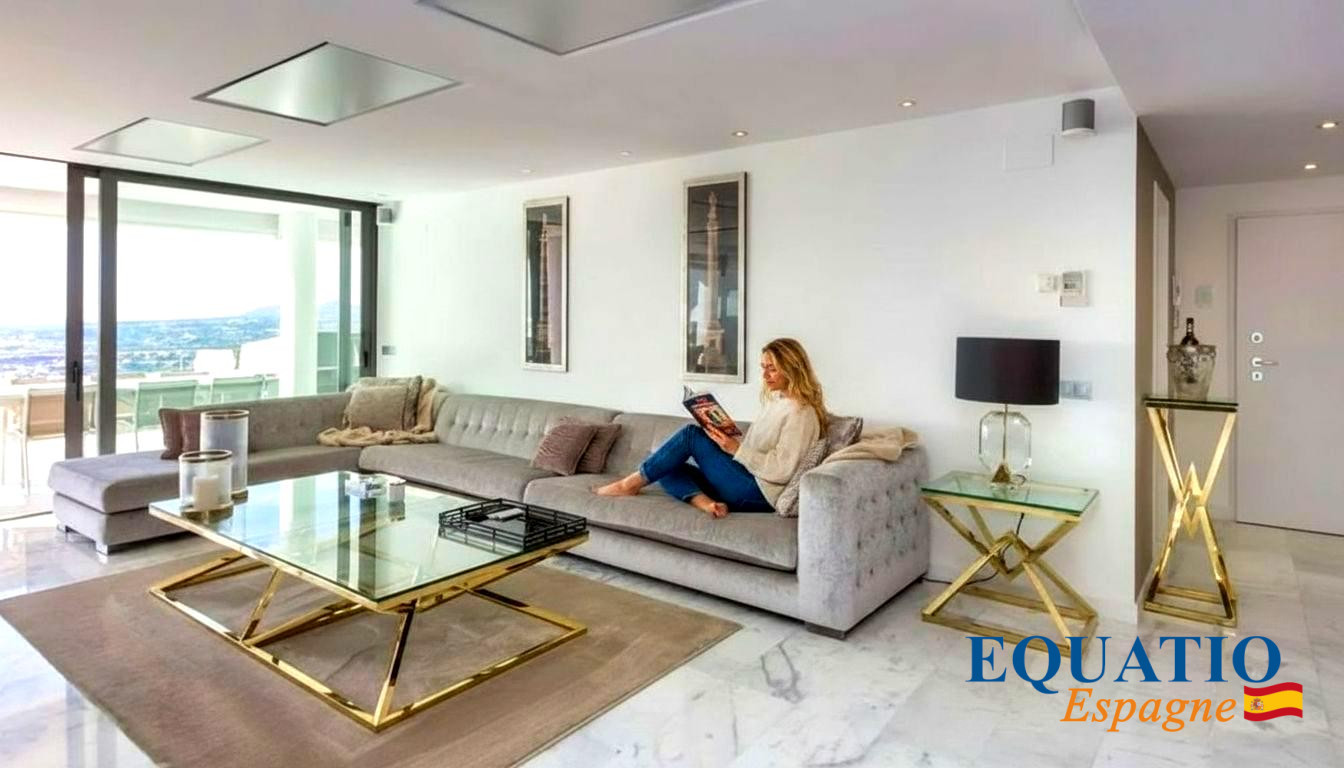 Woman sits on a light gray sectional reading a magazine in a bright, modern living room with a glass-and-gold coffee table.