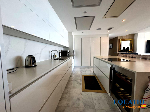 Bright, modern white kitchen with glossy cabinets, marble countertops and floor, a long island with an induction cooktop and sink.