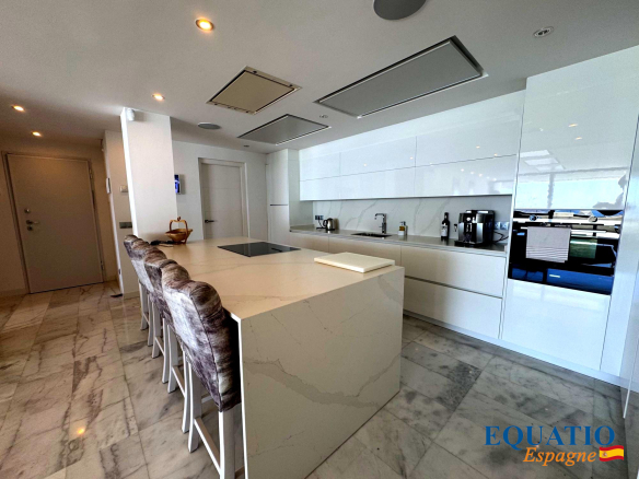 Modern white kitchen with a large marble island, bar stools, and built-in appliances.