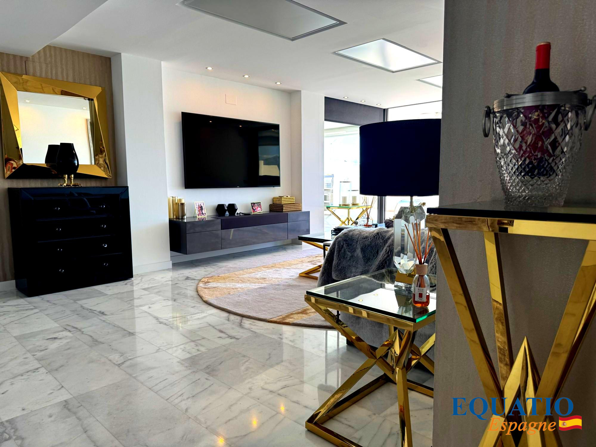 Modern living room with marble floors, white walls, a wall-mounted TV, and a black sleek sideboard with a gold-framed mirror above it.