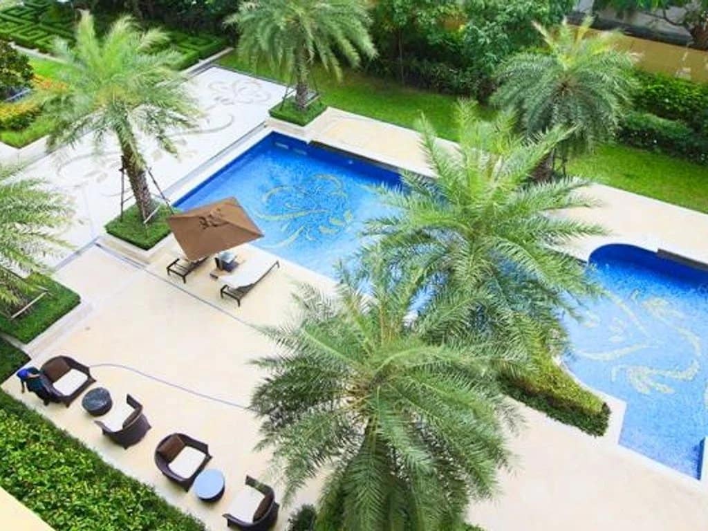 Vue d'une piscine entourée de palmiers dans un appartement de luxe à Bangkok.