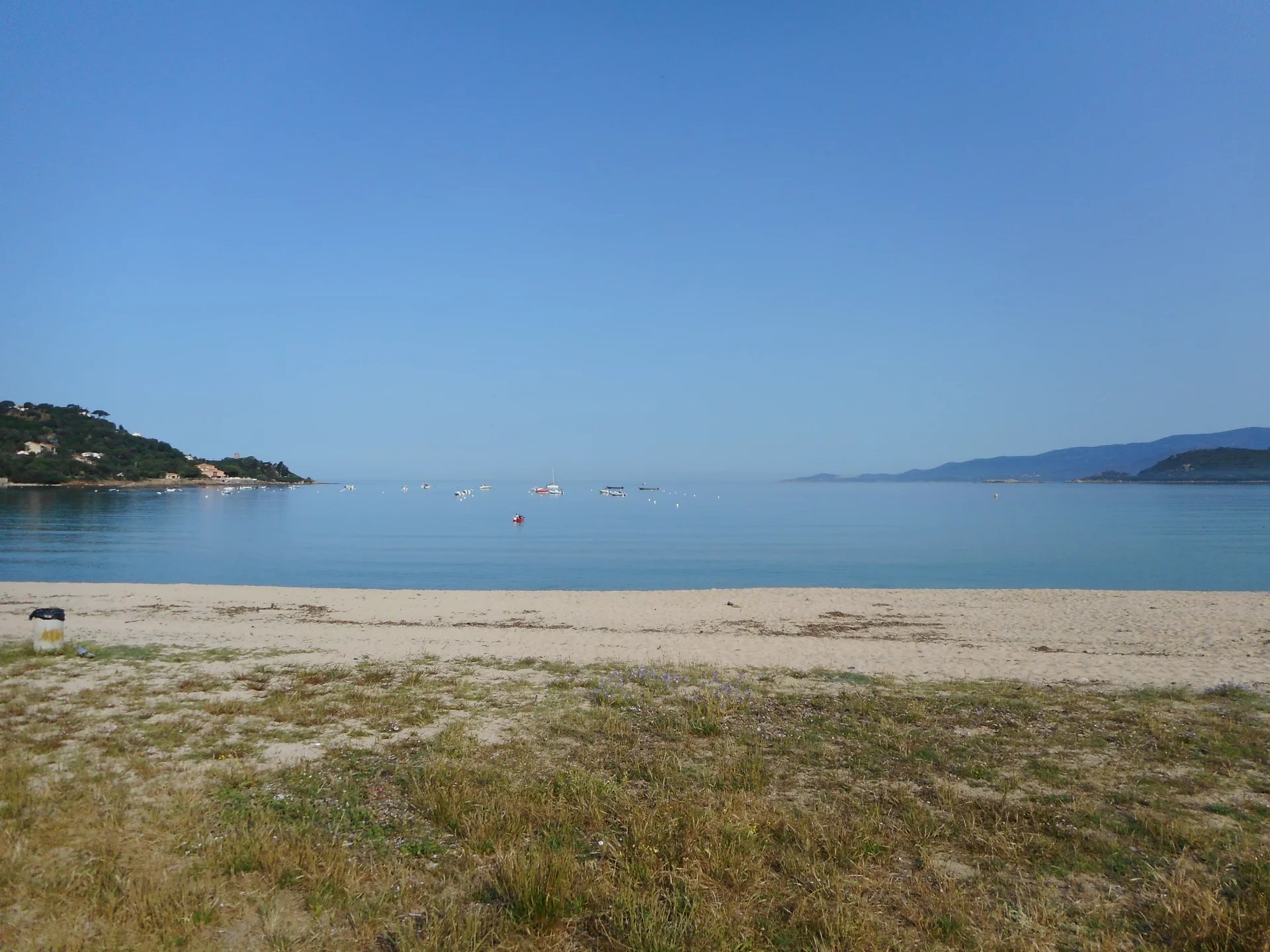 Plage de Calcatoggio Plage calme avec vue sur la mer à Calcatoggio, ciel dégagé et bateaux au loin.
