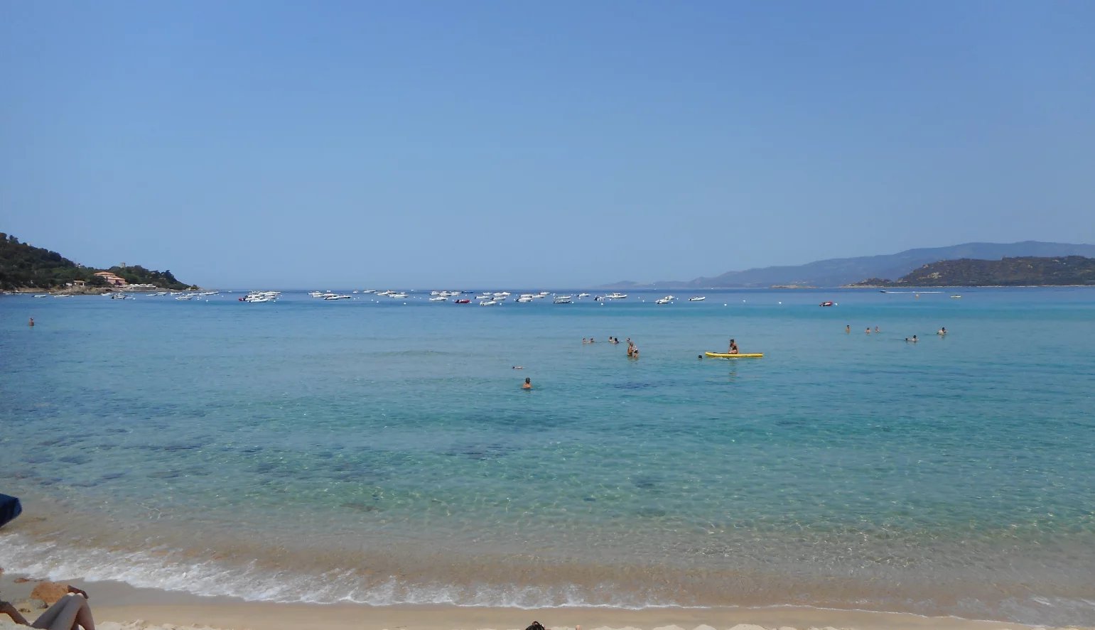 Plage de Calcatoggio Plage de Calcatoggio avec des baigneurs et des bateaux au large, ciel dégagé.
