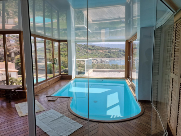 Intérieur d'une villa avec piscine vitrée et vue sur la mer.