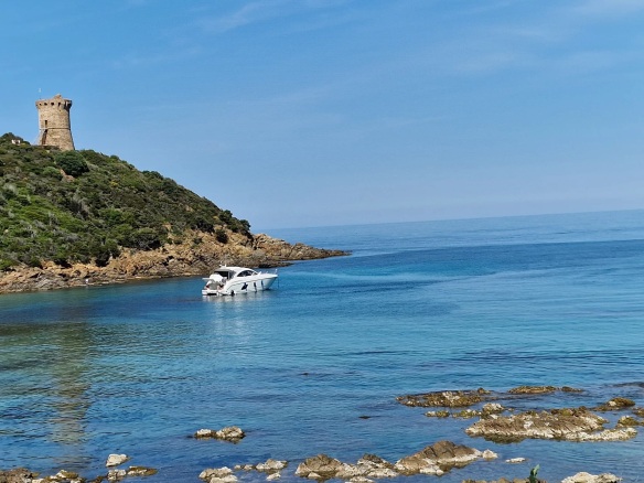 Vue d'un bateau à moteur près d'une côte rocheuse avec une tour au sommet d'une colline.