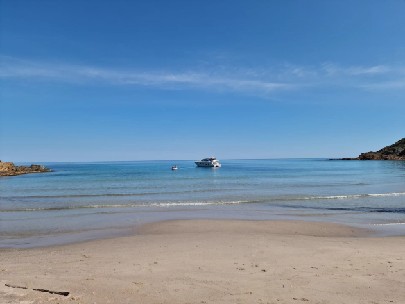 Plage calme avec un bateau au large et ciel dégagé à Conca, côte Fautea.