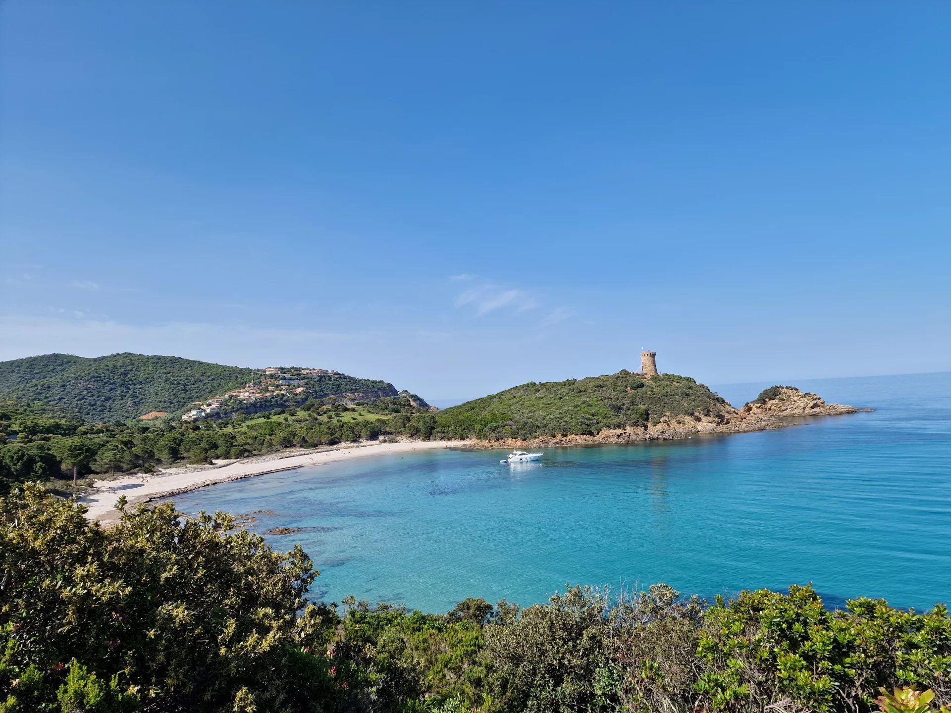 Plage de Fautea Vue panoramique de la plage de Fautea avec une tour en arrière-plan et un bateau sur l'eau.