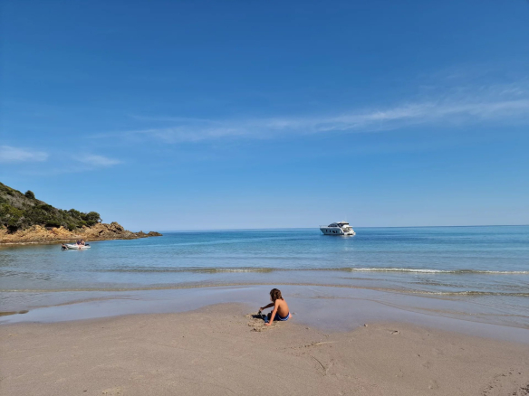 Plage tranquille avec un enfant jouant dans le sable et un bateau au large.