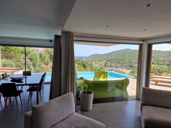 Intérieur d'une villa moderne avec vue sur la mer et la montagne, piscine à débordement visible.