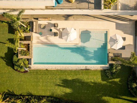 Vue aérienne d'une piscine entourée de pelouse et de parasols dans une propriété de luxe.