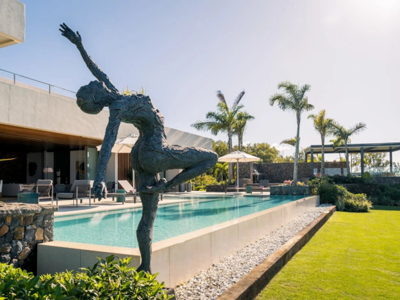 Propriété moderne avec piscine, sculpture et jardin, face à un lagon.