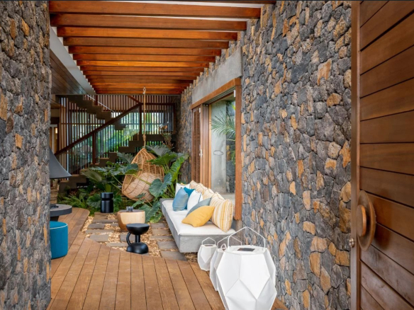 Intérieur d'une propriété moderne avec murs en pierre, mobilier élégant et décoration tropicale.