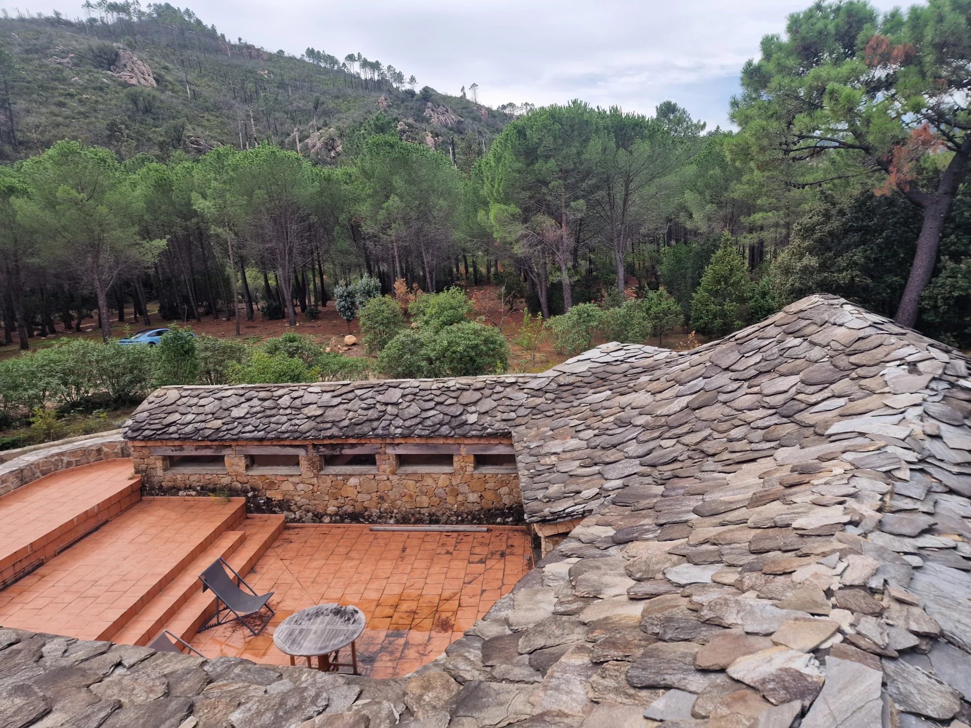 Bastide en pierre à Solenzara Vue de la toiture en pierre d'une bastide avec terrasse et forêt en arrière-plan.