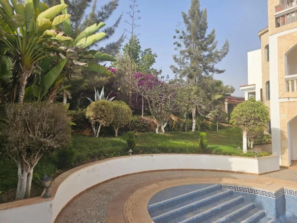 Jardin d'une villa avec piscine, arbres et plantes à Agadir, vue sur la mer et les montagnes.