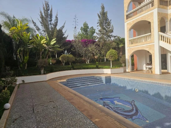 Vue de la piscine et du jardin d'une villa à Illigh, Agadir, avec des plantes et des arbres.