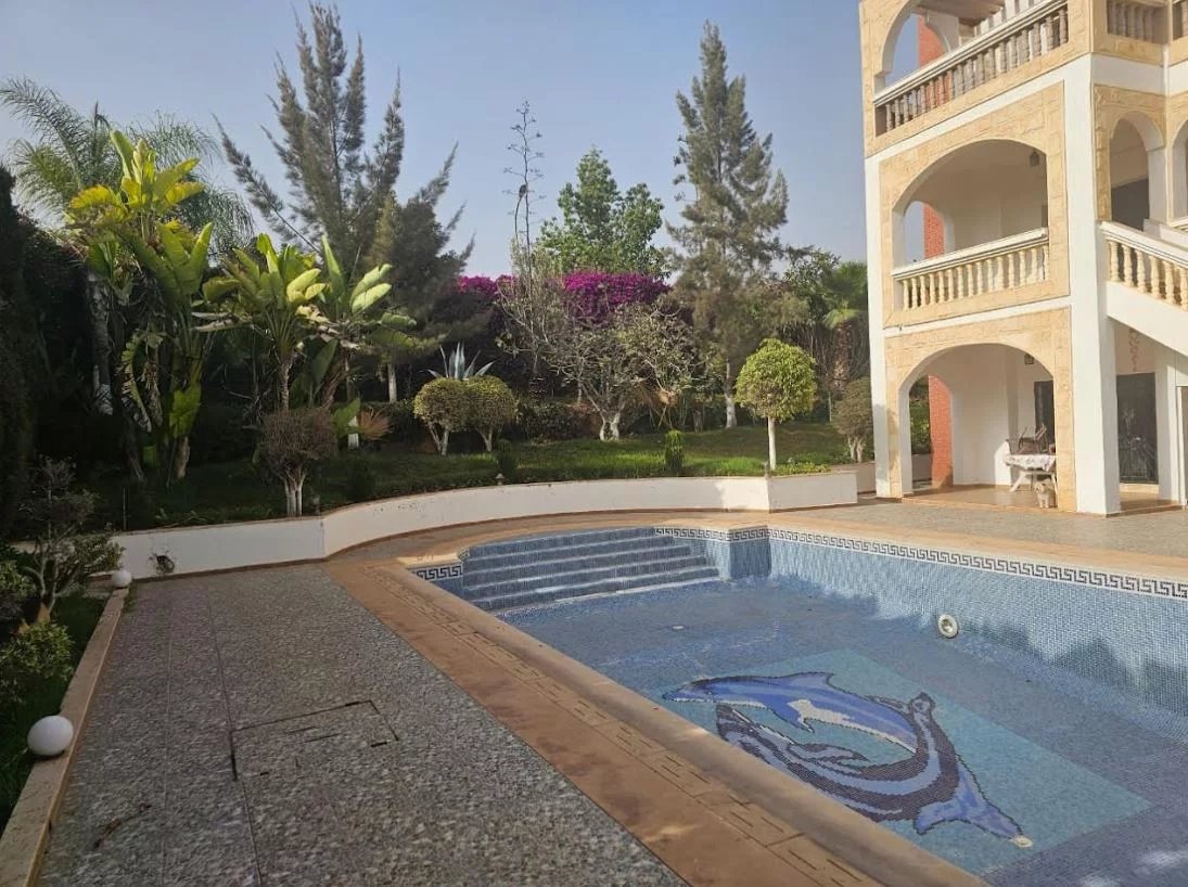 Villa Prestige à Illigh, Agadir Vue de la piscine et du jardin d'une villa à Illigh, Agadir, avec des plantes et des arbres.