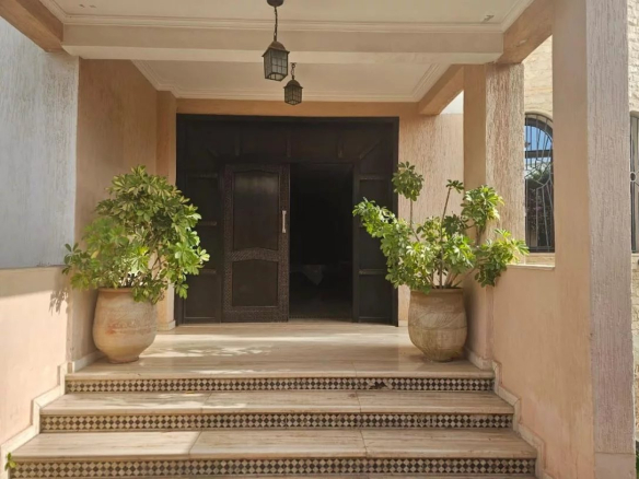 Entrée d'une villa avec des pots de fleurs sur les côtés et une grande porte en bois.
