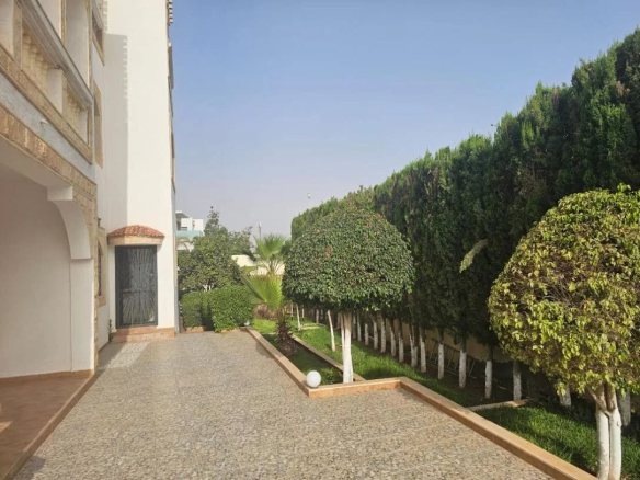 Jardin et allée d'une villa à Illigh, Agadir, avec des arbres bien taillés et un sol en gravier.
