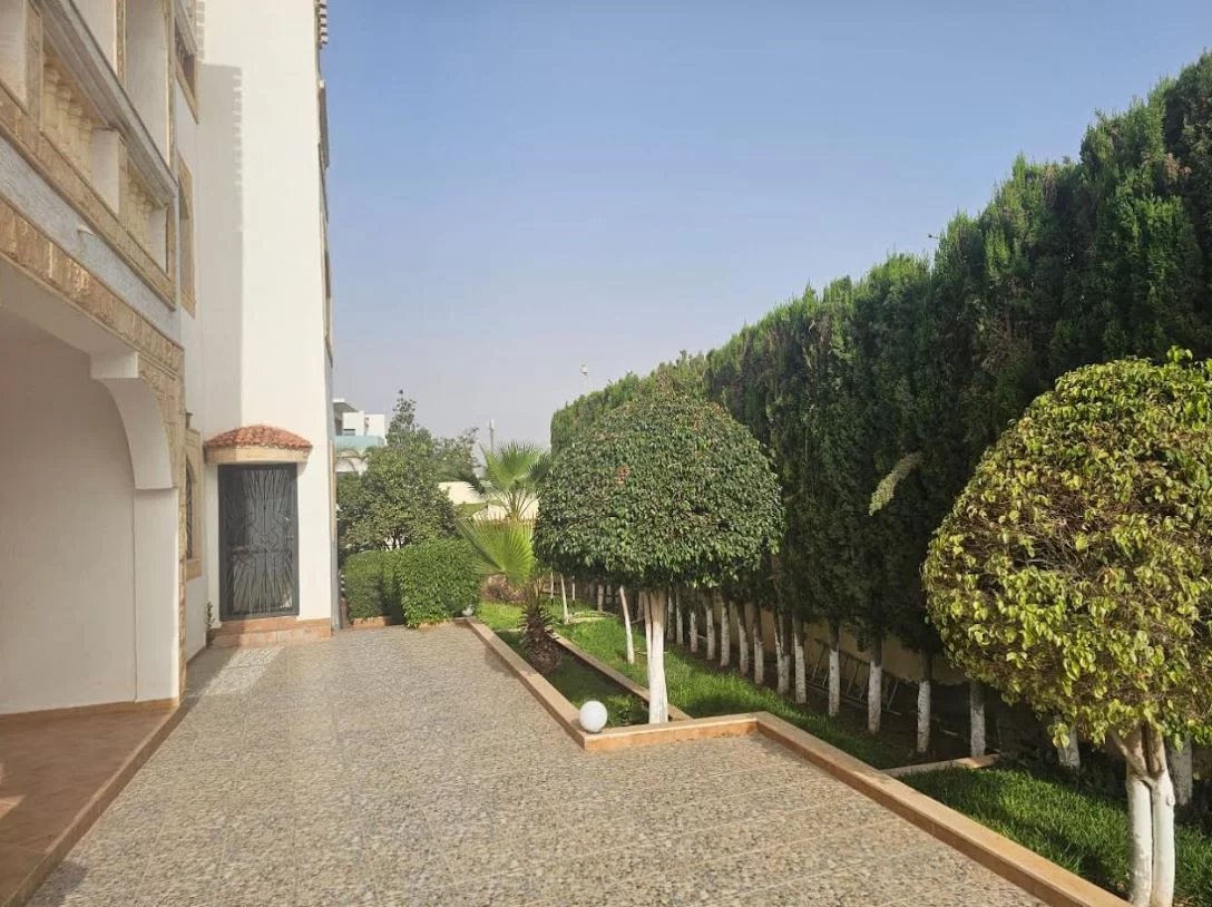 Jardin de la Villa Prestige à Illigh Jardin et allée d'une villa à Illigh, Agadir, avec des arbres bien taillés et un sol en gravier.