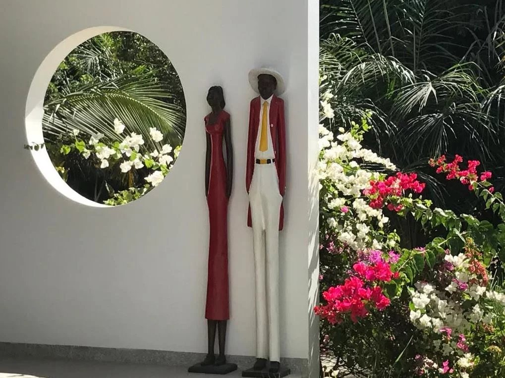 Sculptures décoratives dans un jardin Deux sculptures en métal représentant un homme et une femme, entourées de fleurs colorées.