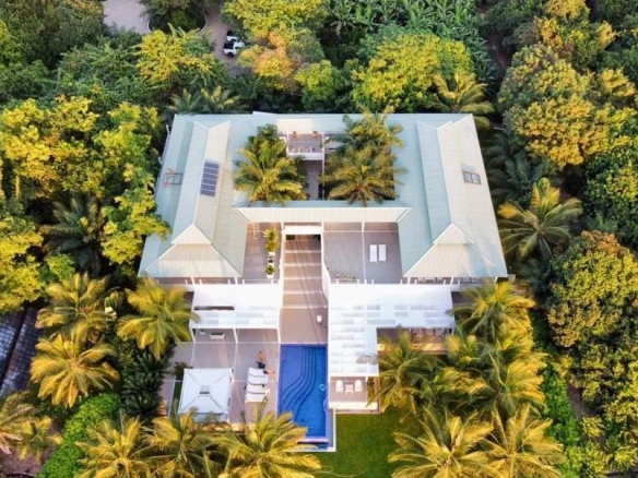 Vue aérienne d'une somptueuse propriété entourée de verdure, avec piscine et accès direct à la plage.