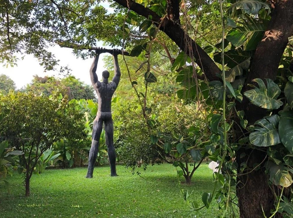 Statue dans un jardin Statue en métal représentant un homme levant un bâton, entourée de verdure dans un jardin.