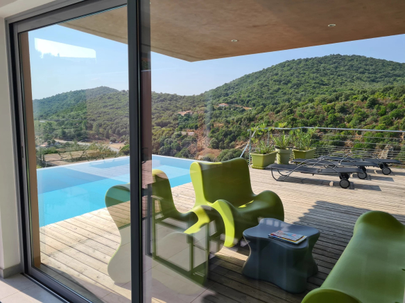 Vue sur la terrasse et la piscine d'une villa d'architecte à Conca, entourée de verdure.