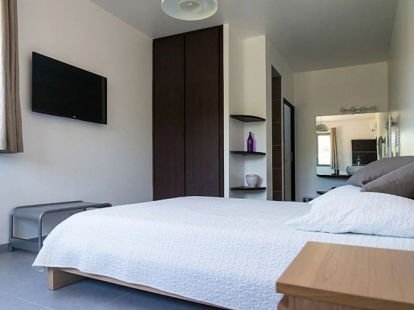 Chambre d'une villa moderne avec lit double et télévision murale.