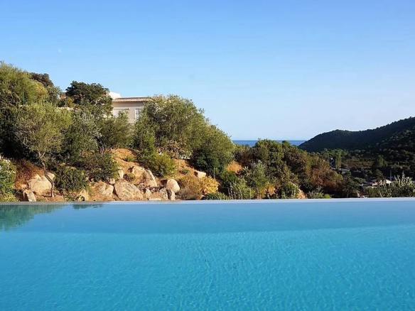 Vue de la piscine à débordement d'une villa d'architecte avec paysage montagneux et vue sur la mer.