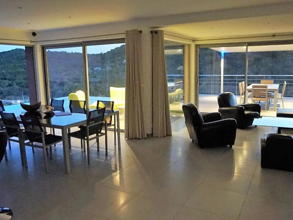 Intérieur d'une villa moderne avec salon et salle à manger, grandes baies vitrées et vue sur la montagne.