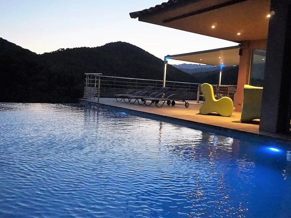 Vue de la piscine à débordement d'une villa d'architecte avec terrasse et montagnes en arrière-plan.