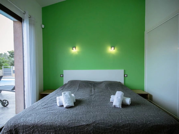 Chambre d'une villa contemporaine avec mur vert et lit double, serviettes blanches sur le lit.